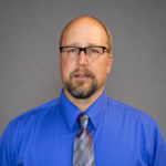 Mike Kutzke wearing a blue dress shirt and gray tie